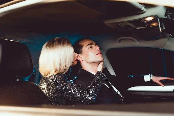 Verführerische junge Frau beißt schönen Mann im Auto ins Ohr — Stockfoto