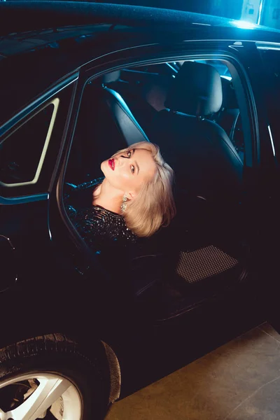 Beautiful fashionable young woman looking at camera while posing in car — Stock Photo