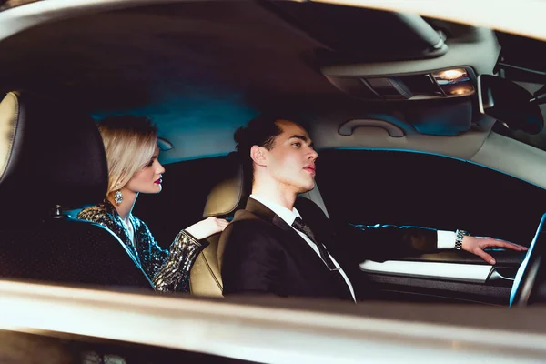 Stylish man and beautiful young woman in formal wear sitting in car — Stock Photo