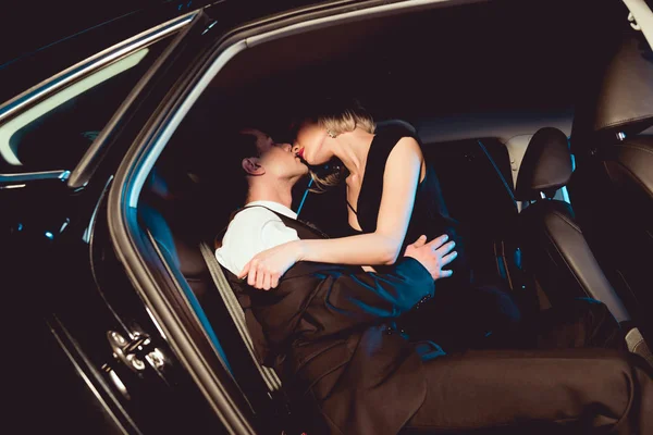 Стильный мужчина целует чувственную молодую женщину в черной машине — стоковое фото
