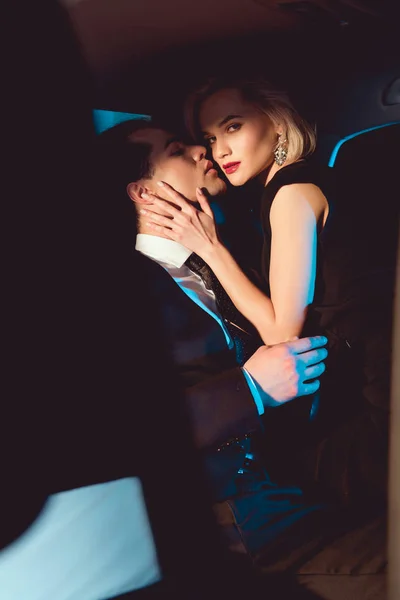 Belle jeune femme à la mode embrassant bel homme et regardant la caméra — Photo de stock