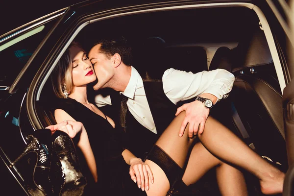 Elegante bonito homem abraçando e beijando sexy menina em meias no carro — Fotografia de Stock