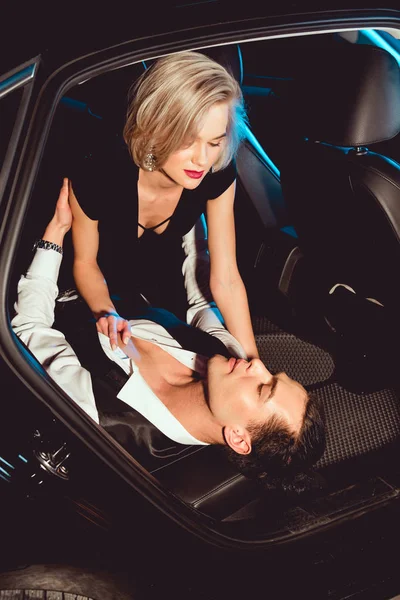 Fashionable young woman undressing handsome man in car — Stock Photo
