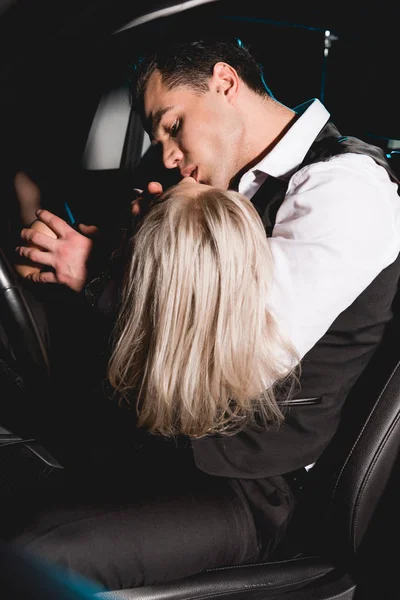 Bel homme en tenue formelle embrasser jeune femme en voiture — Photo de stock