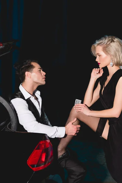 Hombre guapo abrazando pierna de mujer hermosa con condón cerca de coche - foto de stock