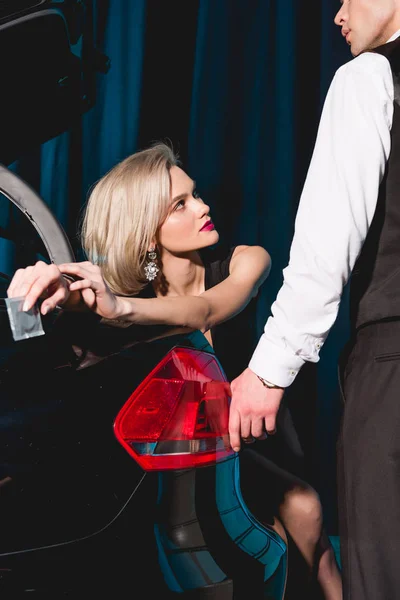 Beautiful young woman holding condom near man and black car — Stock Photo