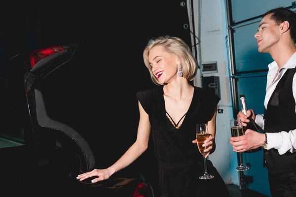 Homme élégant et jeune femme heureuse avec des verres de champagne près de la voiture — Photo de stock