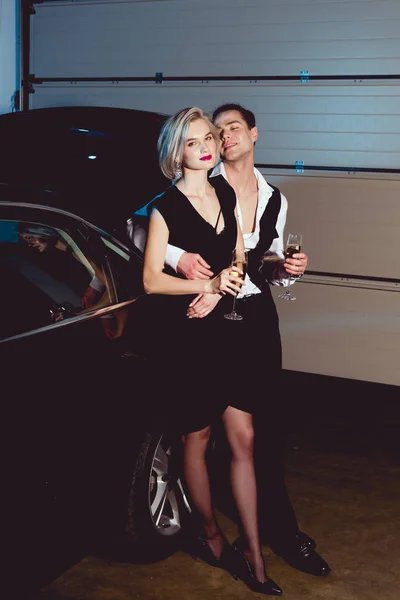 Stylish man and young woman with champagne glasses near car — Stock Photo