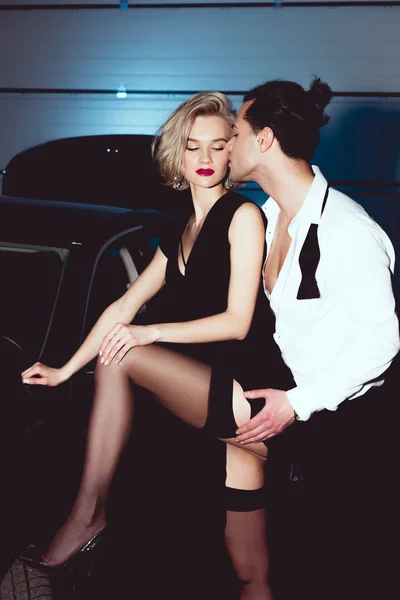 Stylish man kissing beautiful sensual woman in stockings near car — Stock Photo
