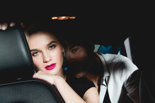 Homme et jeune femme assis sur le siège arrière de la voiture dans l'obscurité et regardant la caméra — Photo de stock