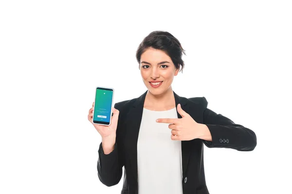 KYIV, UCRAINA - Aprile 24, 2019: Sorridente donna d'affari mista che punta il dito contro lo smartphone con l'app Twitter sullo schermo isolato su bianco . — Foto stock