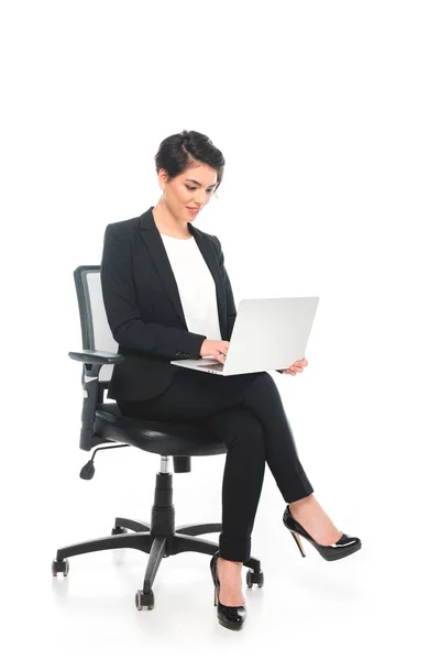 Sonriente mujer de negocios de raza mixta sentado en la silla de la oficina y el uso de ordenador portátil sobre fondo blanco - foto de stock