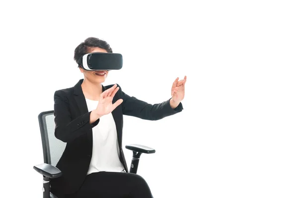 Giovane donna d'affari razza mista gesticolando mentre seduto sulla sedia ufficio e utilizzando cuffia realtà virtuale isolato su bianco — Foto stock