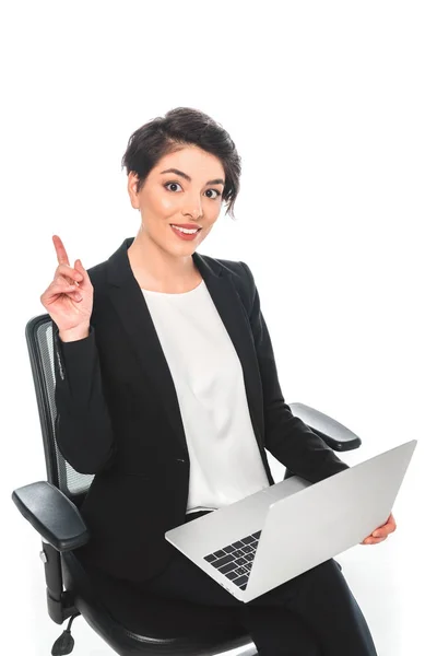 Fröhliche gemischte Geschäftsfrau zeigt Ideenschild, während sie im Bürostuhl sitzt und Laptop isoliert auf Weiß benutzt — Stockfoto