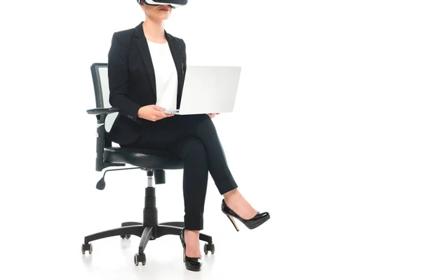 Vista parcial de la mujer de negocios de raza mixta utilizando auriculares de realidad virtual mientras está sentado en la silla de la oficina y el uso de ordenador portátil sobre fondo blanco - foto de stock