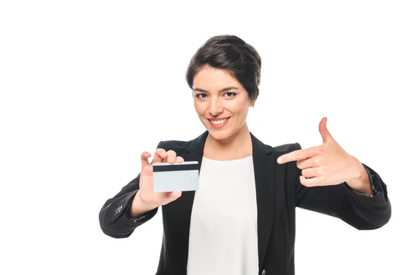 Alegre mista empresária apontando com o dedo para o cartão de crédito e olhando para a câmera isolada no branco — Fotografia de Stock