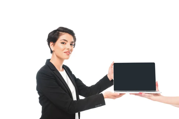 Vista parcial de la mujer que toma el ordenador portátil con la pantalla en blanco de la sonriente mujer de negocios de raza mixta aislada en blanco - foto de stock