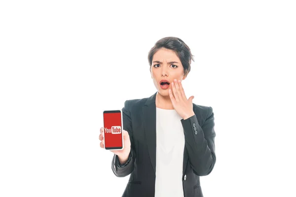 KYIV, UKRAINE - APRIL 24, 2019: Surprised mixed race businesswoman holding smartphone with Youtube app on screen isolated on white. — Stock Photo