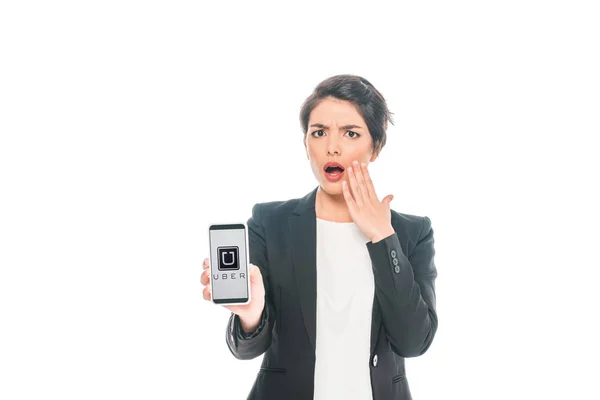 KYIV, UKRAINE - APRIL 24, 2019: Surprised mixed race businesswoman showing smartphone with Uber app on screen isolated on white. — Stock Photo
