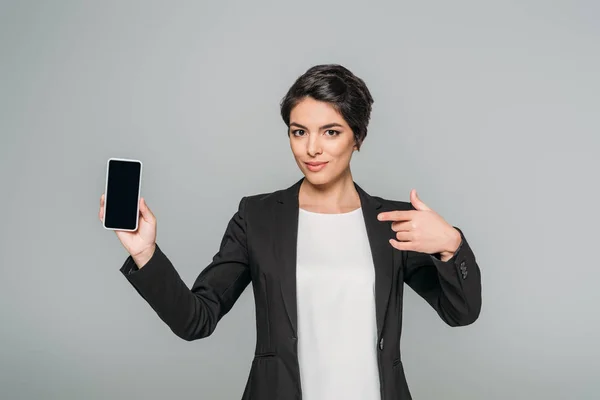 Atraente mista empresária apontando com o dedo para o smartphone com tela em branco isolado no cinza — Fotografia de Stock