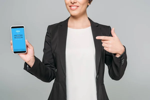KYIV, UCRANIA - 24 DE ABRIL DE 2019: Recorte de la mujer de negocios de raza mixta mostrando el teléfono inteligente con la aplicación de Skype en la pantalla aislada en gris . - foto de stock
