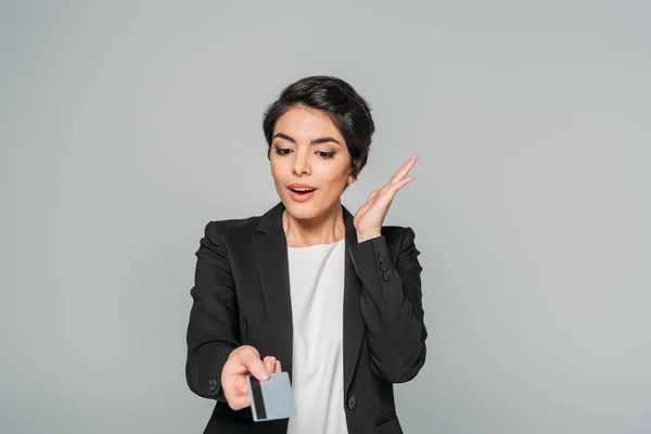 Amused mixed race businesswoman gesturing while holding credit card isolated on grey — Stock Photo