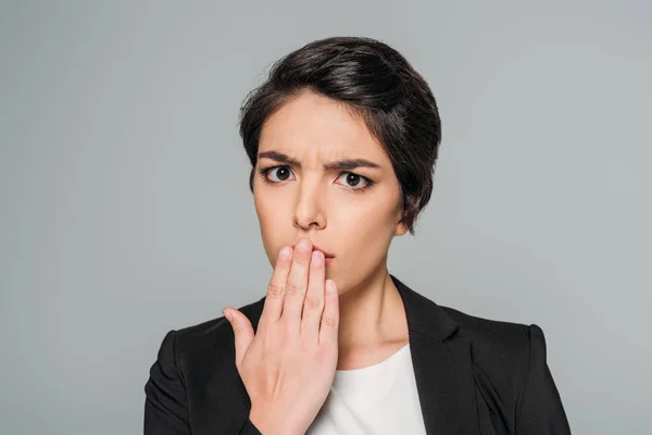 Schockierte Mischlingsunternehmerin bedeckt Mund mit Hand isoliert auf grau — Stockfoto