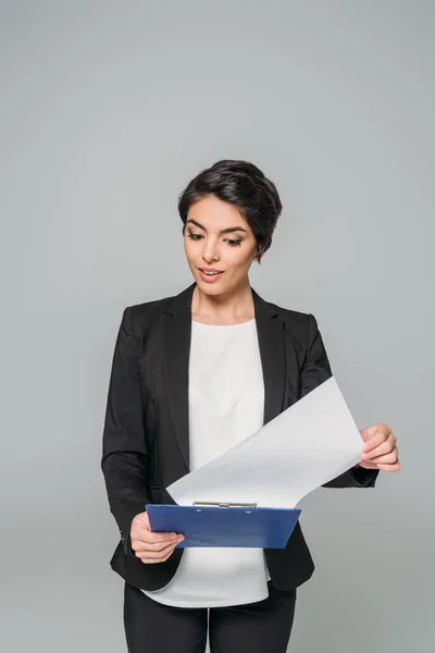 Überrascht gemischte Rasse Geschäftsfrau hält Blick auf Papier auf Klemmbrett isoliert auf grau — Stockfoto