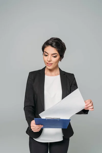 Surpris mixte femme d'affaires tenant regardant le papier sur presse-papiers isolé sur gris — Photo de stock