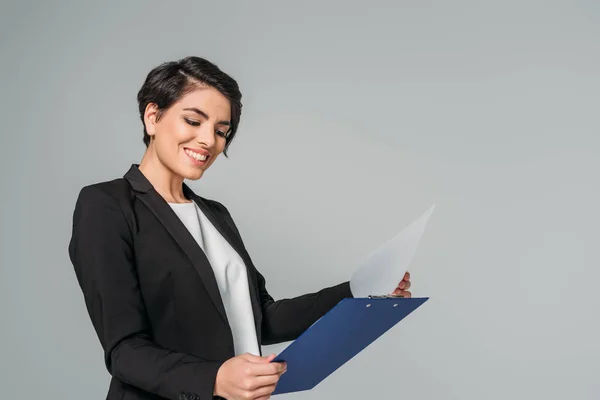 Young mixed race excited businesswoman looking at clipboard isolated on grey — Stock Photo