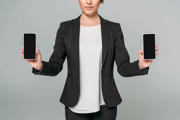 Vue recadrée de jeune femme d'affaires métissée tenant des smartphones avec écran blanc isolé sur gris . — Photo de stock