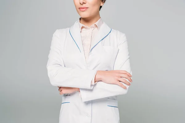 Cropped shot of mixed race doctor in white coat posing at camera with crossed arms isolated on grey — Stock Photo