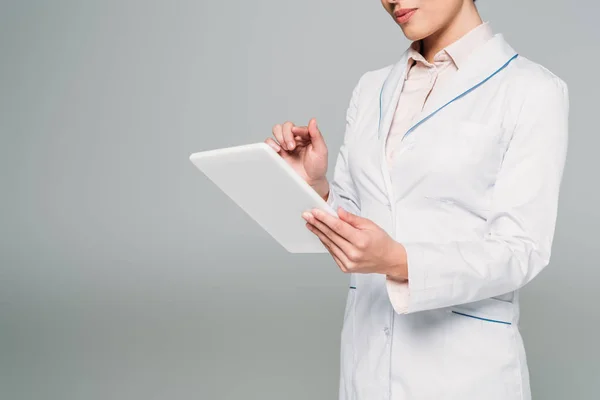 Обрізаний знімок змішаного гоночного лікаря в білому пальто з використанням цифрового планшета ізольовано на сірому — стокове фото