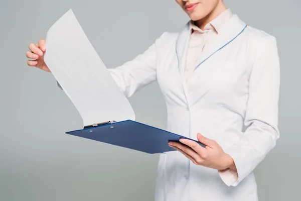 Cropped shot of mixed race doctor looking at clipboard with papers isolated on grey — Stock Photo