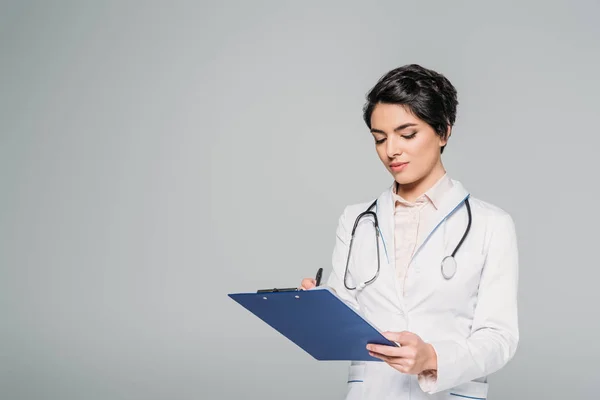 Concentré mixte médecin écriture sur presse-papiers isolé sur gris — Photo de stock