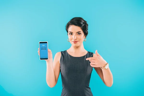 KYIV, UCRANIA - 24 DE ABRIL DE 2019: Bastante mujer de raza mixta mostrando teléfono inteligente con aplicación de Skype en la pantalla aislada en azul . - foto de stock