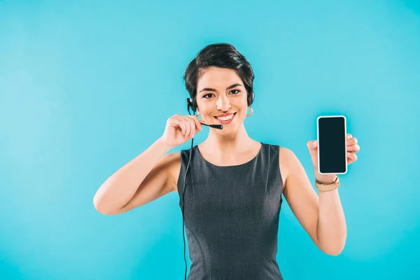 Sonriente operador de centro de llamadas de raza mixta en auriculares que muestran teléfono inteligente con pantalla en blanco aislado en azul - foto de stock