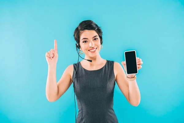 Attractive mixed race call center operator showing idea sign and holding smartphone with blank screen isolated on blue — Stock Photo