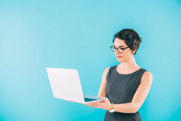 Beautiful mixed race businesswoman in glasses using laptop isolated on blue — Stock Photo