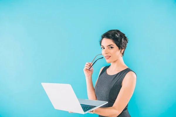 Jolie mixte femme d'affaires tenant ordinateur portable tout en regardant la caméra isolée sur bleu — Photo de stock