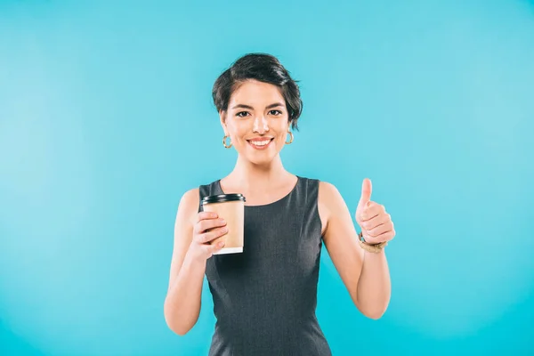 Cheerful mixed race woman showing thumb up while holding paper cup isolated on blue — Stock Photo