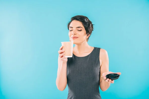 Attraktive Frau mit gemischter Rasse genießt den Geschmack von Kaffee mit geschlossenen Augen, während sie eine Papptasse auf blauem Hintergrund hält — Stockfoto