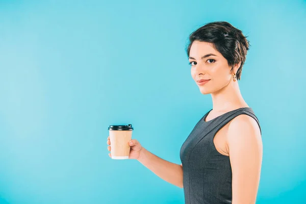 Bastante mujer de raza mixta sosteniendo la taza de papel mientras mira a la cámara en fondo azul - foto de stock