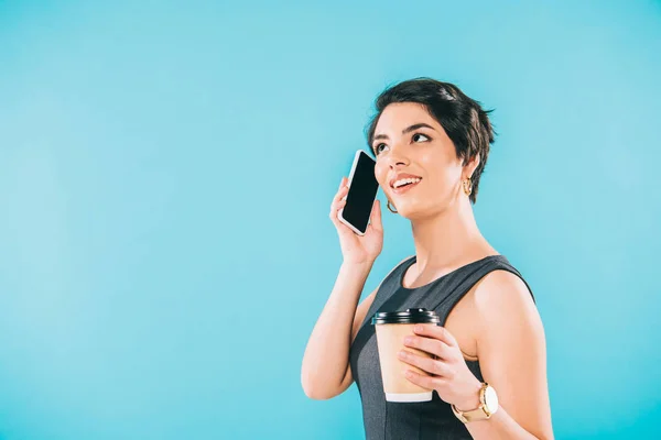 Alegre mulher de raça mista falando no smartphone enquanto segurando copo de papel isolado no azul — Fotografia de Stock