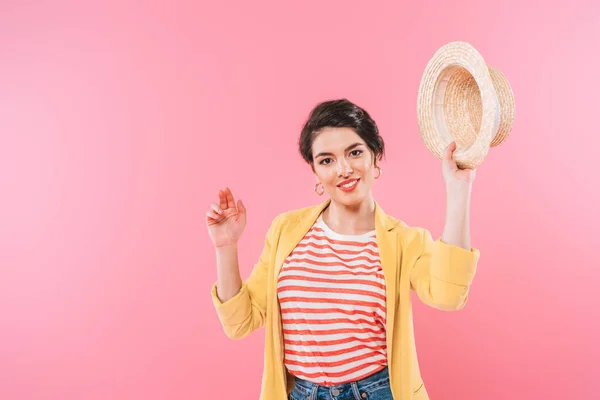 Bonita mujer de raza mixta agitando sombrero de paja y sonriendo a la cámara aislada en rosa - foto de stock