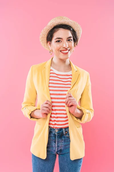 Attractive mixed race woman in bright clothing and straw hat smiling at camera isolated on pink — Stock Photo