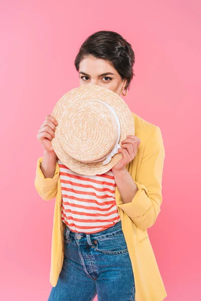 Pretty mixed race woman covering face with straw hat isolated on pink — Stock Photo