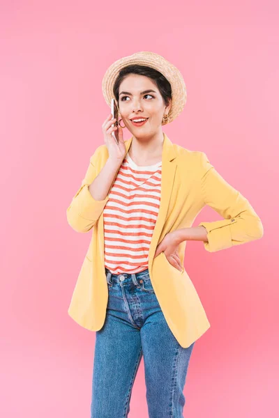 Alegre chica de raza mixta hablando en el teléfono inteligente mientras toma de la mano en la cadera sobre fondo rosa - foto de stock