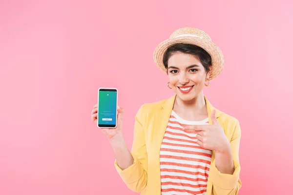 KYIV, UKRAINE - APRIL 24, 2019: Pretty mixed race woman showing smartphone with Twitter app on screen isolated on pink. — Stock Photo