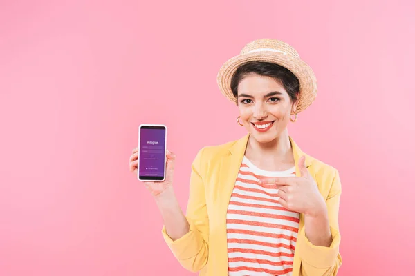 KYIV, UKRAINE - 24 AVRIL 2019 : Femme souriante mixte montrant smartphone avec application Instagram à l'écran isolé sur rose . — Photo de stock